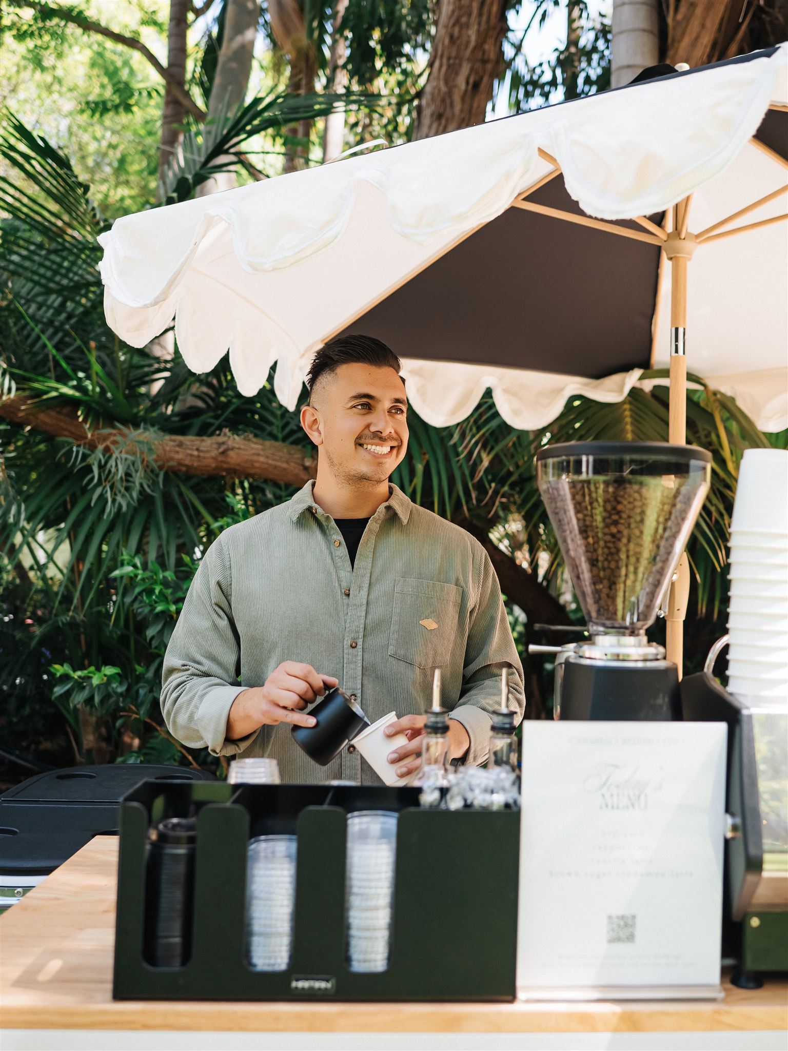 Barista standing behind the bar of a coffee cart serving hot and iced lattes for a wedding